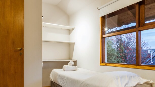 A bedroom with a single bed, a wooden door, and a window with a view of trees and a building.
