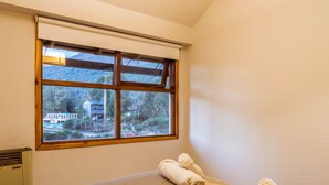 A room with a large window, a bed, and a pair of towels on the bed.