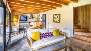 Una sala de estar acogedora con techo de madera, un sofá con cojines, una mesa de centro y vistas al área de cocina y comedor.