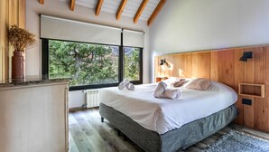 Un dormitorio con una cama grande, cabecera de madera, ventana con vistas a árboles y piso de madera.