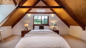 Une chambre avec un plafond en pente, un lit, deux tables de chevet et une fenêtre donnant sur un paysage verdoyant.