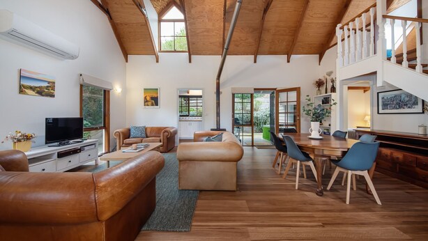 Un vaste espace de vie doté d’un haut plafond, d’une cheminée, d’un coin repas avec une table et des chaises en bois, et d’un téléviseur posé sur un meuble blanc.