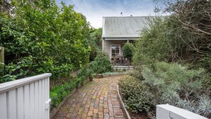 Un chemin menant à une maison dont le toit est fait de tôle ondulée, entourée d’une végétation luxuriante et d’une clôture en bois.