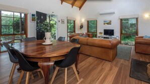 Un salon moderne avec une table à manger en bois, des canapés en cuir et de grandes fenêtres donnant sur un paysage verdoyant.