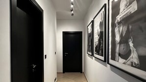 A hallway with a tiled floor, black doors, and framed pictures on the walls. - Trendy Seaside Escape |Designer Finished Penthouse

 (Wied il-Ghajn)