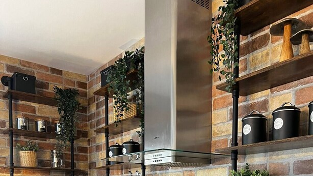 A modern kitchen with exposed brick walls, wooden shelves, and a built-in microwave. - Trendy Seaside Escape |Designer Finished Penthouse

 (Wied il-Ghajn)