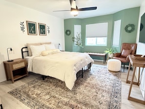 Quarto com cama, mesas de cabeceira, uma cadeira, escrivaninha e ventilador de teto.