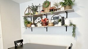 Et spiseområde med et mørkt træbord og stole, med to sorte hylder med pynt og planter på hver side.
