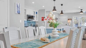 A modern kitchen with white cabinets, a dining area with white chairs, and a central island with a vase of flowers. - 3BR Wildwood Crest Family Home - Easy walk 2 beach (Wildwood Crest)
