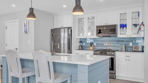 A modern kitchen with white cabinets, a central island with bar stools, stainless steel appliances, and pendant lighting. - 3BR Wildwood Crest Family Home - Easy walk 2 beach (Wildwood Crest)