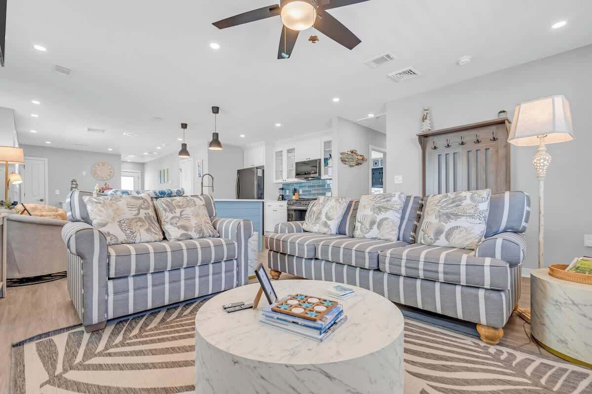 A spacious living room with striped sofas, a marble coffee table, and a ceiling fan.
