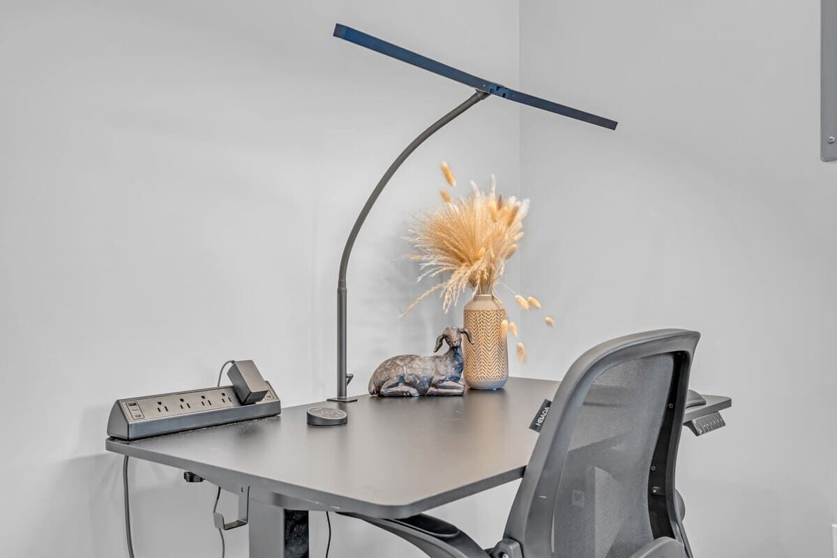 Un bureau moderne doté d’une multiprise, d’une lampe, d’un vase contenant des plantes séchées et d’un objet décoratif.