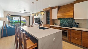 A modern kitchen with a large island, wooden cabinets, and pendant lighting.