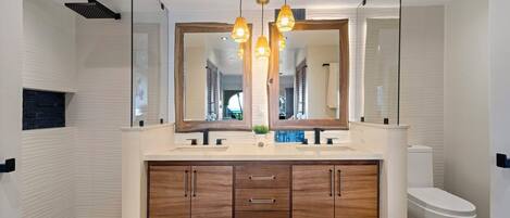 Un baño moderno con un espejo grande, tocador de madera y zona de ducha.
