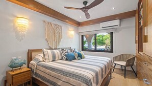 A bedroom with a bed, bedside tables, a ceiling fan, wall sconces, a window, and a chair.