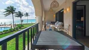 A balcony with a view of the ocean, a pool, and palm trees.