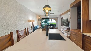 A modern kitchen with a large island, wooden chairs, a hanging light fixture, and a view of the outdoors.