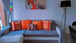 Un salon moderne avec un canapé gris, des coussins orange et à carreaux, et un lampadaire.