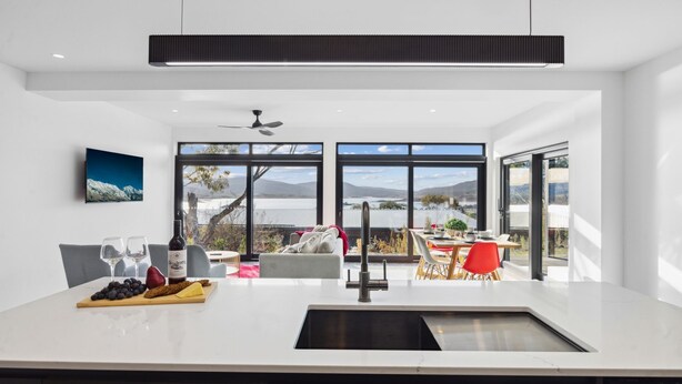 Una cocina moderna con una isla central, ventanas amplias que ofrecen una vista panorámica y un comedor con sillas rojas.