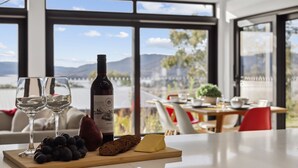 Una mesa con una botella de vino Shiraz, dos copas, uvas, una hogaza de pan y un trozo de queso.