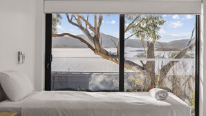 Un dormitorio con un amplio ventanal que ofrece vistas a un lago y montañas.