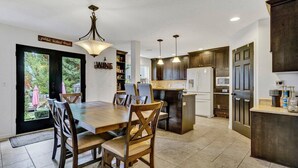 A modern kitchen with a dining area, featuring a large wooden table, dark cabinets, and pendant lighting. - Cozy Fall Retreat w/ Swim Spa (Tigard)