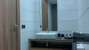 Ein modernes Badezimmer mit Holztür, weißen Fliesenwänden, einem weißen Waschbecken und einer Toilette.