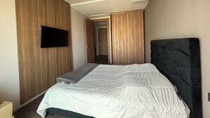 Ein modernes Schlafzimmer mit Bett, Holzwandverkleidung, einem Flachbildfernseher und Einbauleuchten.