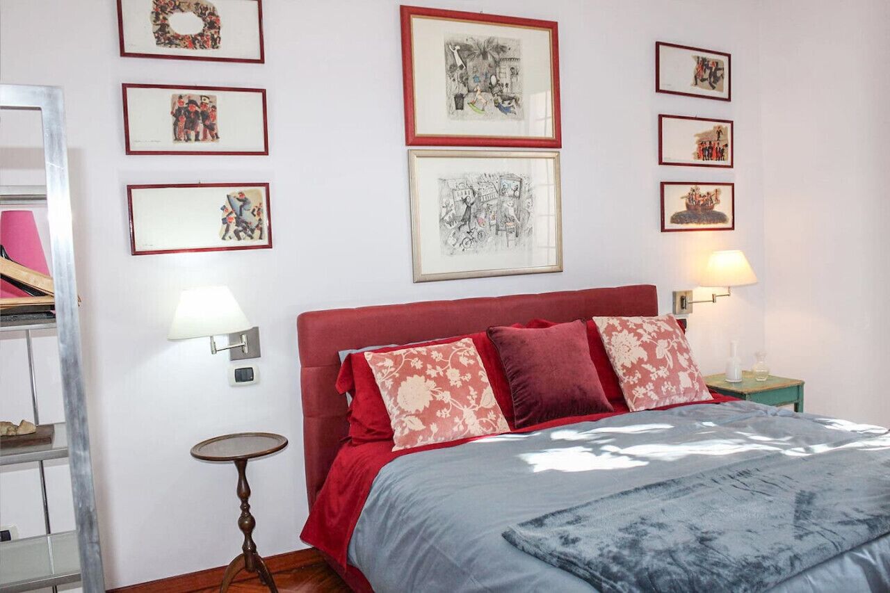 Ein Schlafzimmer mit einem roten Kopfteil, einem Bett mit roter und blauer Bettwäsche, einem kleinen runden Tisch und Wandlampen.