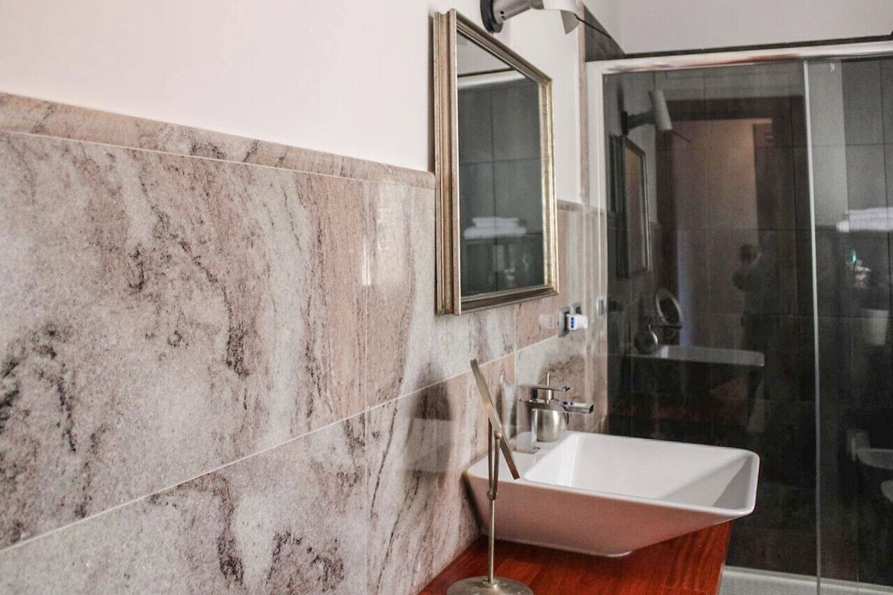 A bathroom with a marble wall, a sink, and a glass shower enclosure.