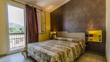 Relax in a spacious room with a large bed, sliding glass door to a balcony, and views of the surrounding greenery and mountains.