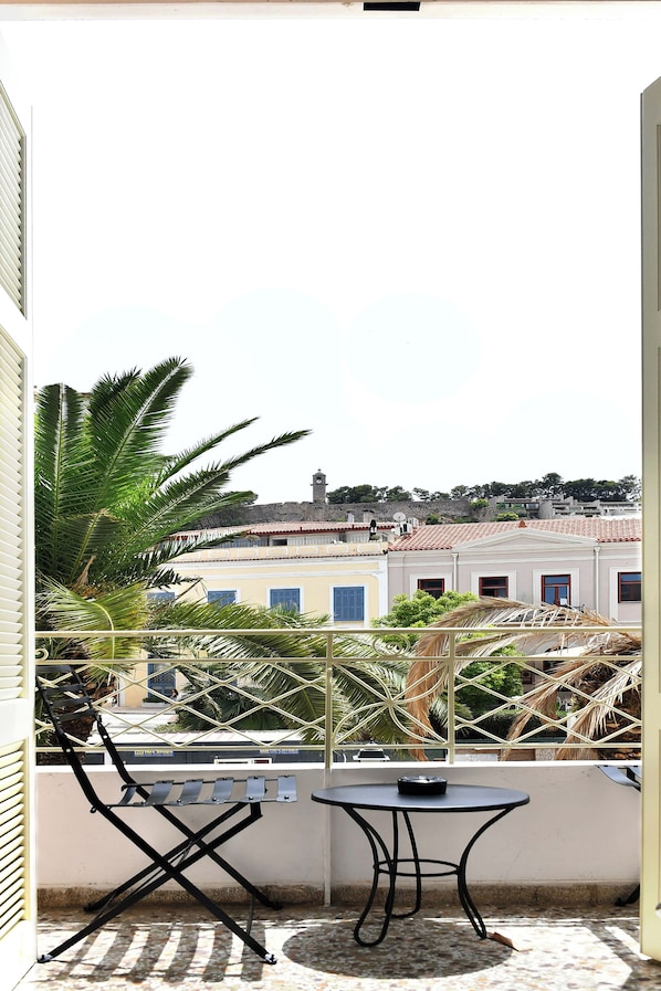 A balcony with a table and chairs, overlooking a cityscape with buildings and a hill in the background. - Porto Nafplio (Nafplio)