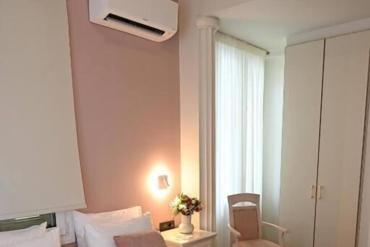 A hotel room with two beds, a chair, a wardrobe, and an air conditioning unit.