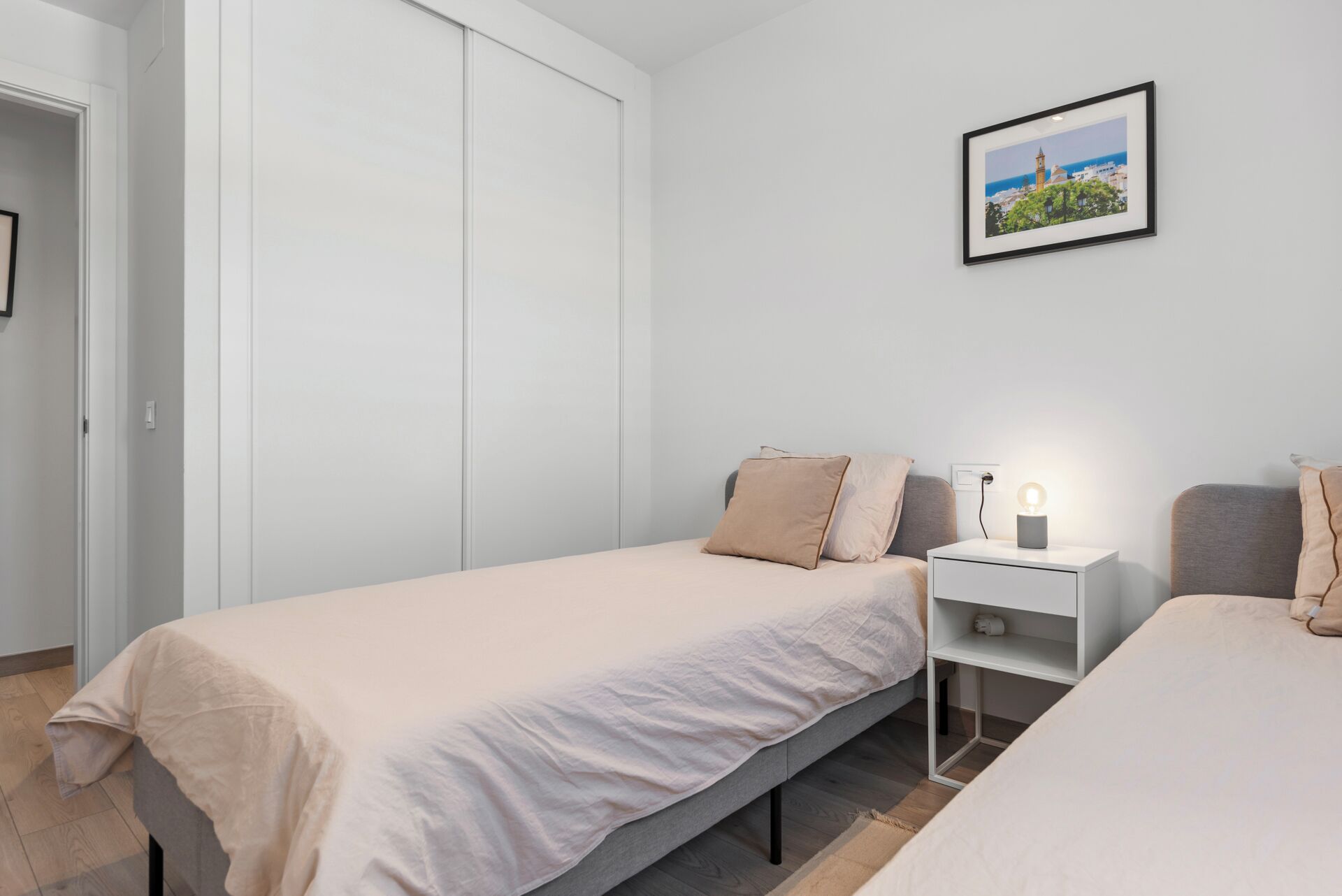 Ein Schlafzimmer mit zwei Einzelbetten, einem Nachttisch mit Lampe und einem gerahmten Bild an der Wand.