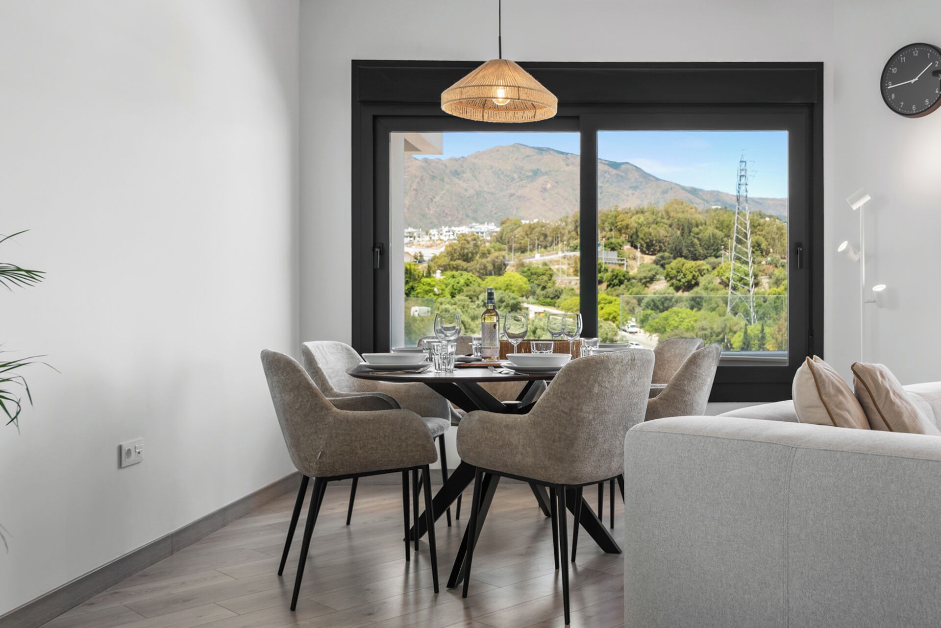 A dining area with a table set for four, a sofa, and a large window with a mountain view.
