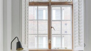 Ein Zimmer mit einem Holztisch, einem grauen Bürostuhl, einer hölzernen Kommode und einem Fenster mit weißen Fensterläden.