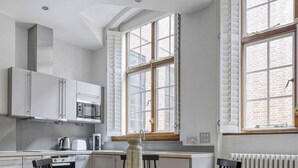 Eine moderne Küche mit weißen Schränken, einem runden Holztisch und schwarzen Stühlen.