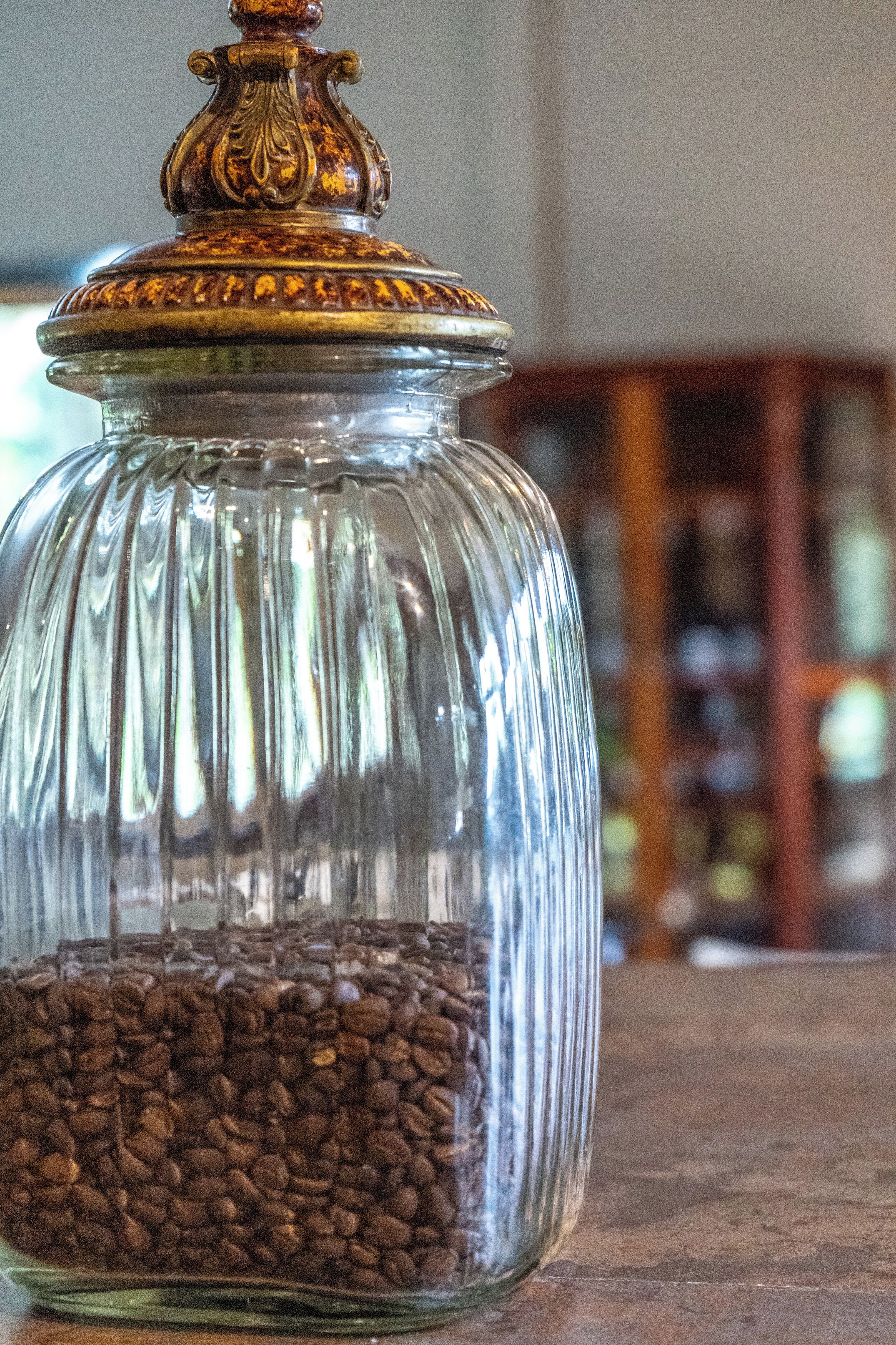 A glass jar filled with coffee beans, placed on a wooden surface.