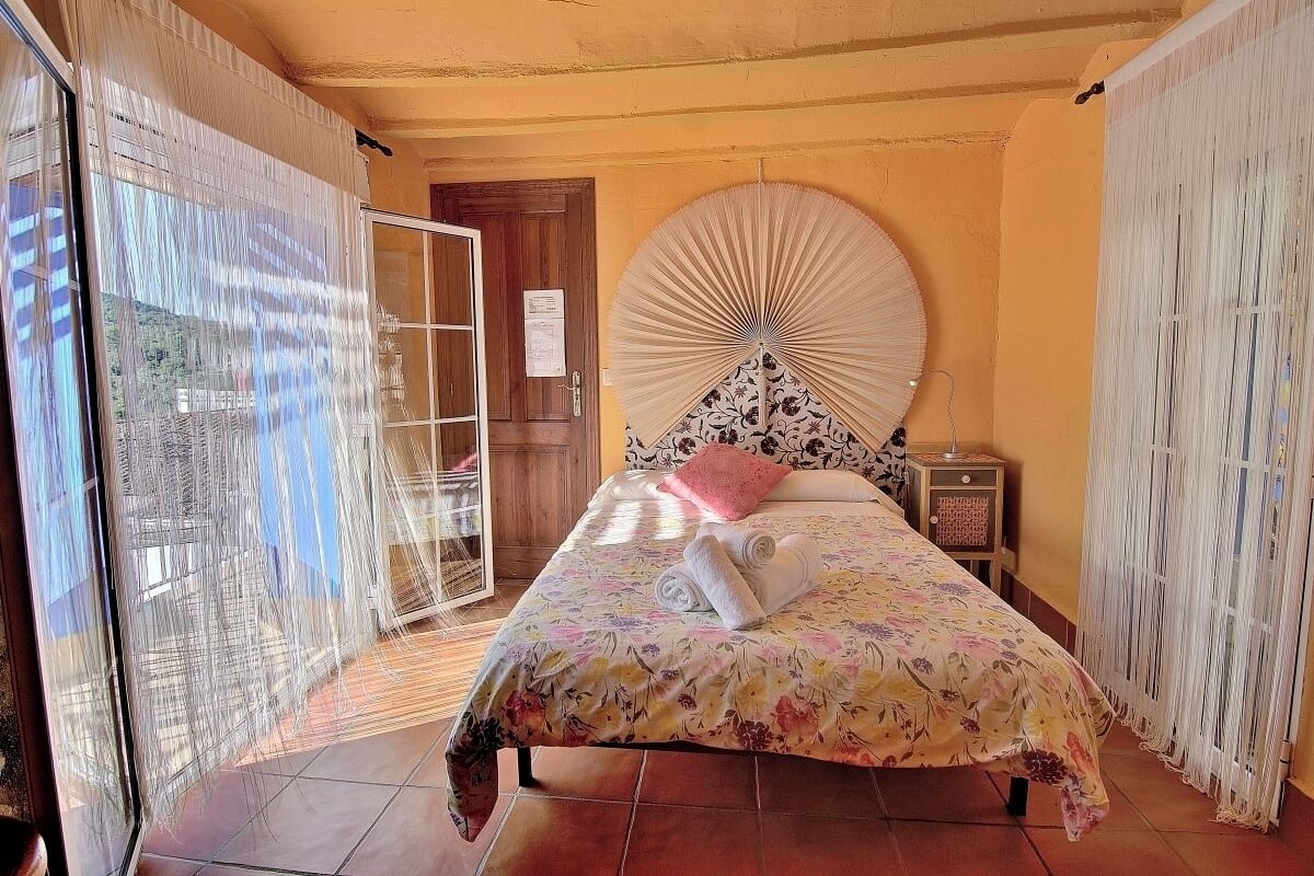 A bedroom with a bed, a nightstand, a wall fan, and a door.