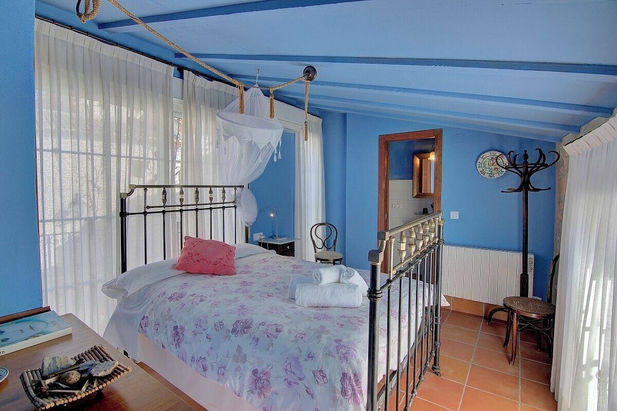 A bedroom with a bed, a bedside table, a chair, a mirror, and a coat rack.