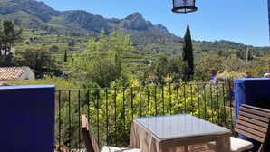 Una terraza con vistas a montañas, una mesa, sillas y un farol colgante.