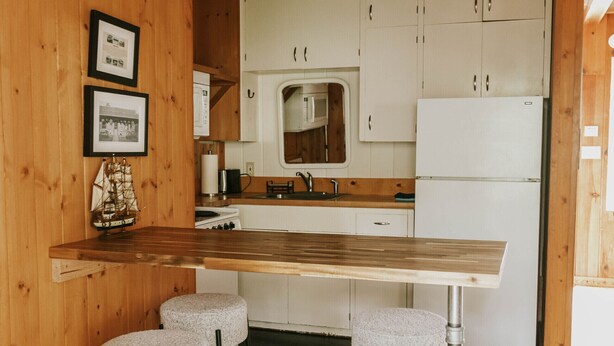 A kitchen with wooden cabinets, a white refrigerator, and a bar area with stools. - Full Property Buyout (Arch Cape)