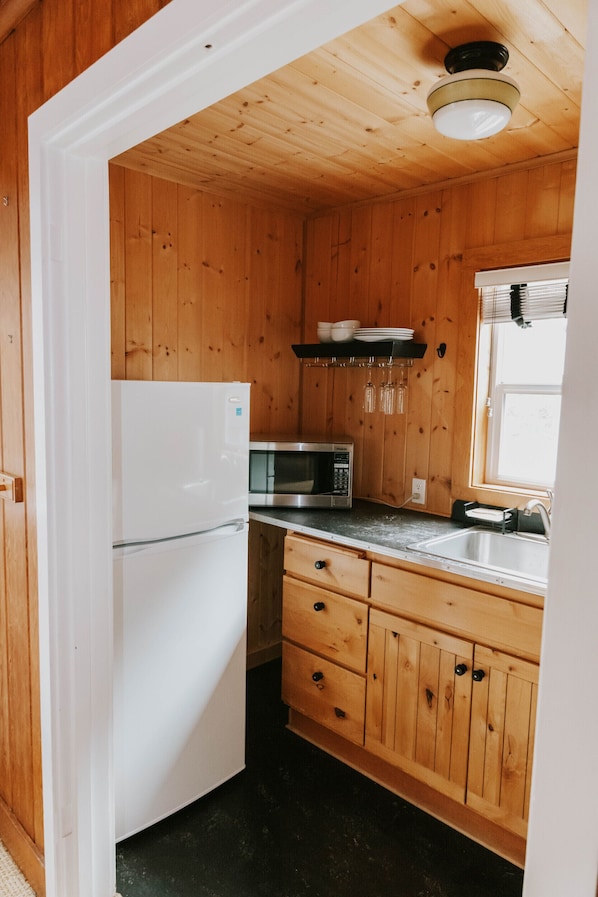 A compact kitchen with wooden walls, a white refrigerator, a microwave, and a sink. - The Inn at Arch Cape (Arch Cape)