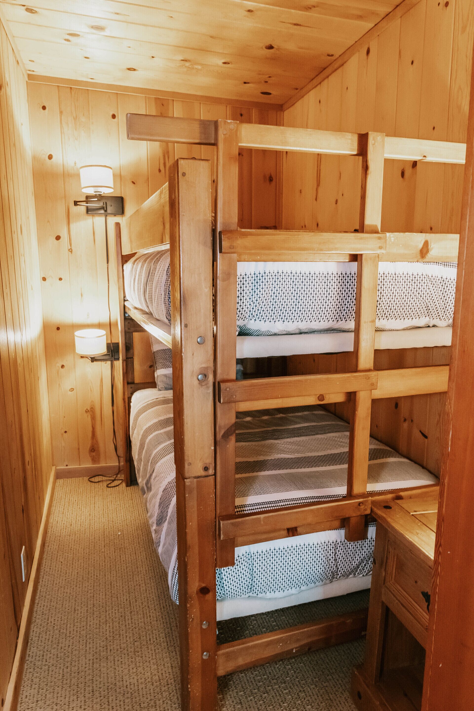 A wooden bunk bed room with a carpeted floor and a wall-mounted light fixture.