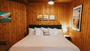 A wooden-paneled room with a bed, a nightstand, and wall art. - Full Property Buyout (Arch Cape)