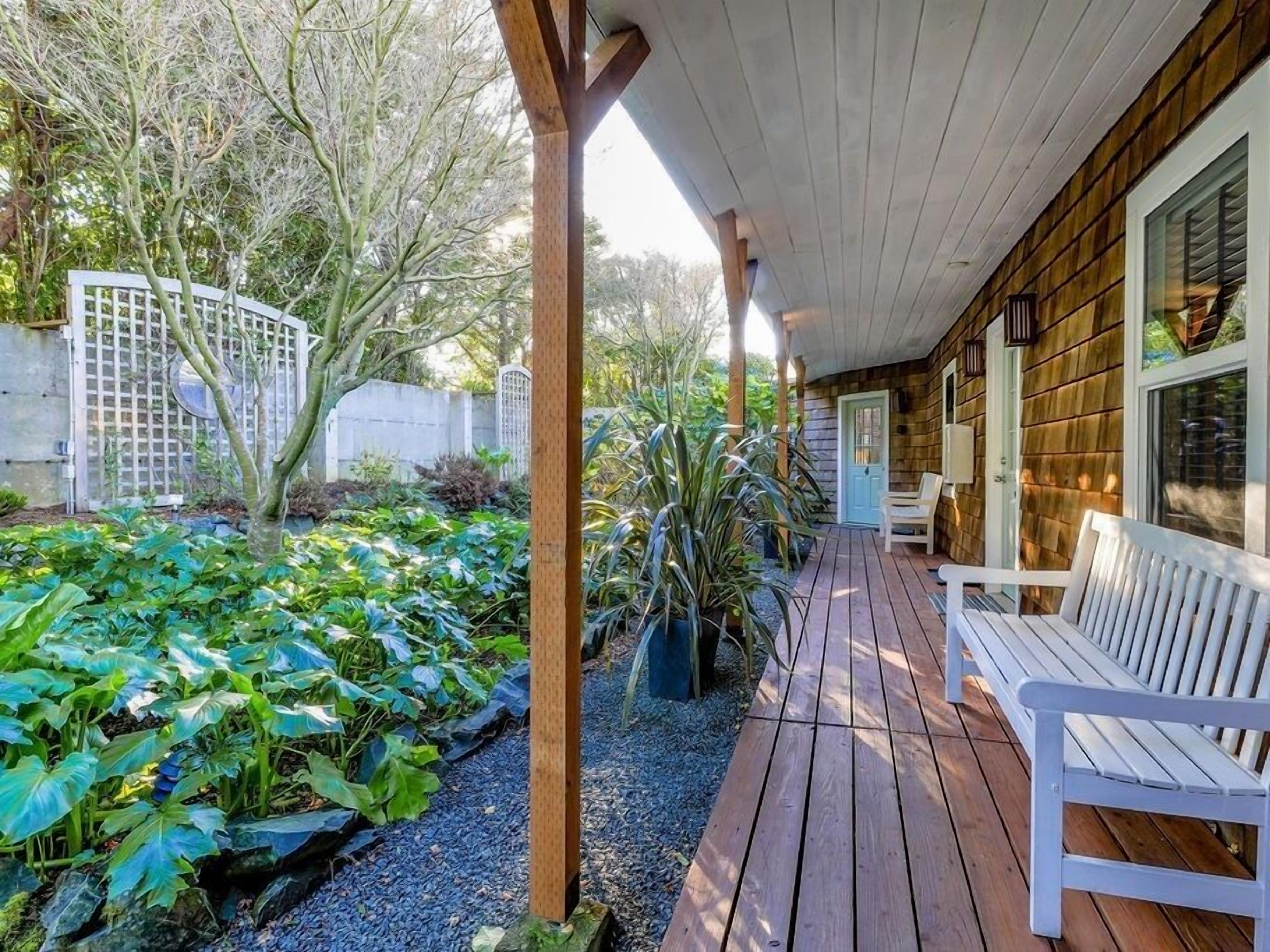 Eine Holzterrasse mit einer Bank, umgeben von einem Garten mit verschiedenen Pflanzen und einem weißen Zaun.