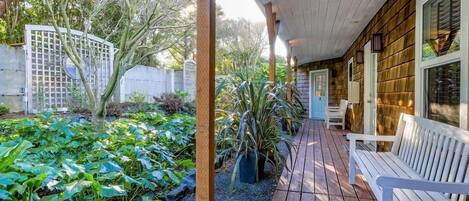 Eine Holzterrasse mit einer Bank, umgeben von einem Garten mit verschiedenen Pflanzen und einem weißen Zaun.