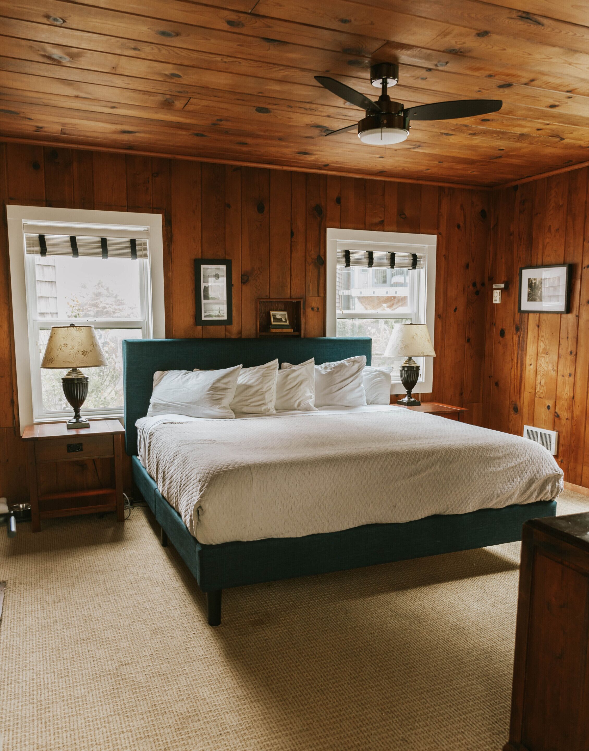 A bedroom with a bed, two bedside tables, a ceiling fan, and wooden walls.