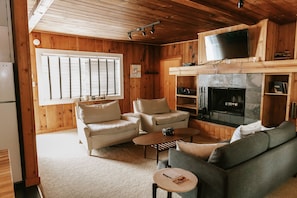 A cozy cabin interior with wooden walls, a fireplace, a television, and a seating area with a sofa and chairs. - The Inn at Arch Cape (Arch Cape)
