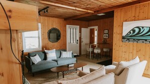 A cozy room with a wooden ceiling, a gray sofa, a beige sofa, a coffee table, and a painting on the wall. - Full Property Buyout (Arch Cape)